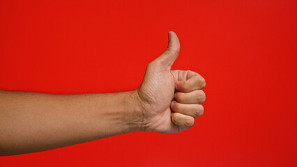 Man's hand showing thumbs up against a vibrant red background, conveying approval and positivity...