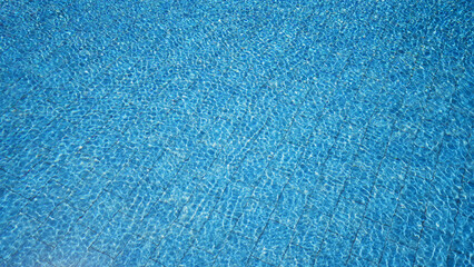 A tranquil blue swimming pool with ripple patterns reflecting sunlight