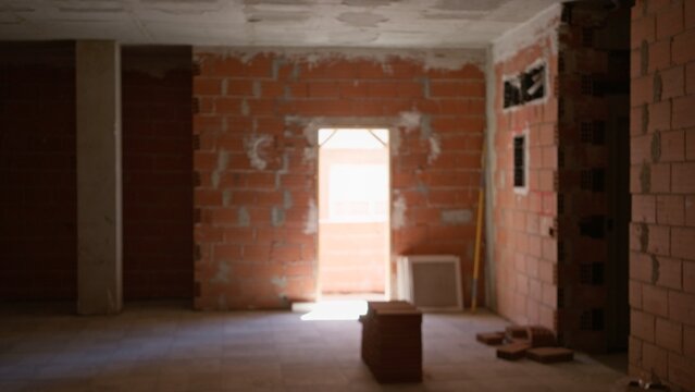 Defocused view of unfinished construction site with exposed brick walls, scattered building materials, and sunlight streaming through an open doorway