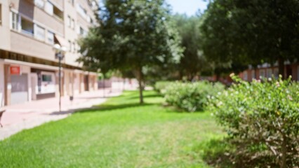 Fototapeta premium Blurred outdoor scene with defocused buildings, trees, bushes, and grass in a sunny urban setting