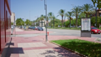 Obraz premium Blurred image of an outdoor street with trees, buildings, palm trees, sidewalk, and a blurry background in a sunny setting.