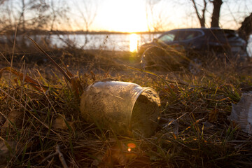 Discarded plastic waste in a natural environment by a car near a lake. Emphasizes environmental pollution, human impact on nature, and the need for sustainable behavior