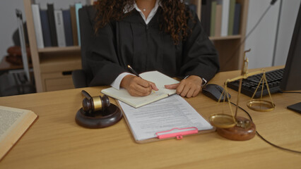 Hispanic woman judge working in an office, writing notes with gavel and legal documents on desk