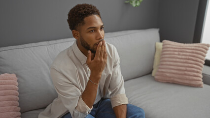 Young man thinking in a living room with stylish decor and soft pillows