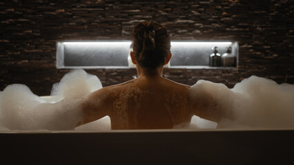 A serene woman enjoys a bubble bath in a tranquil, modern bathroom setting, conveying relaxation and self-care.