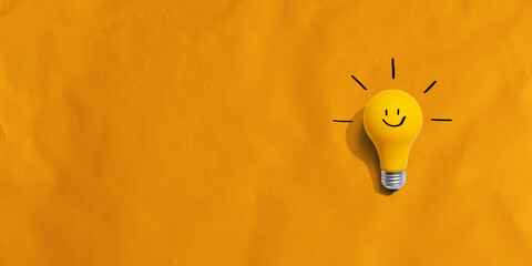 Yellow light bulb with happy face - flat lay