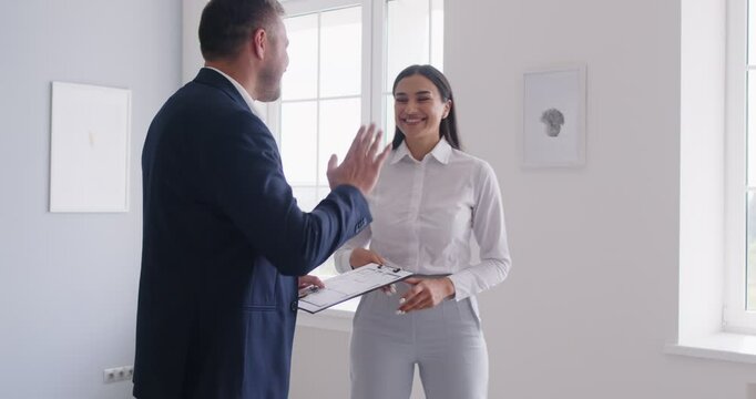 Realtor enthusiastically hands over keys to client after agreeing on details of real estate contract. Female client and male agent give each other high five showing sense of satisfaction and joy.