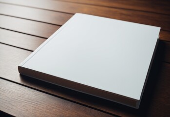 Fototapeta premium A minimalist photo mockup of a clean, white, empty textbook lying on a wooden table. The cover should be smooth and untouched. The pages inside the textbook should be perfectly white and clean