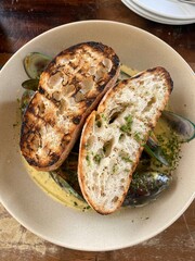 Steamed mussels with white wine, garlic, parsley and cream, grilled bread in the bowl on the wooden table 