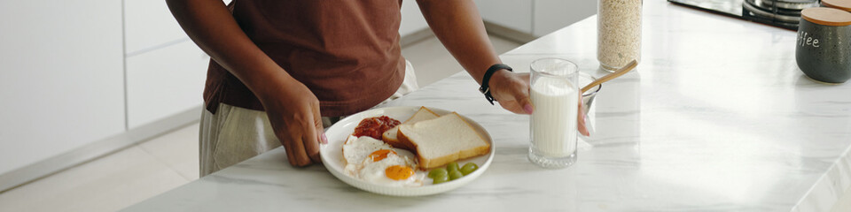 Person preparing nutritious breakfast with toast, eggs, and fruits on a white countertop in a sleek modern kitchen environment without visible face