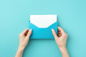 Fototapeta premium person holding blue envelope with white letter inside, set against turquoise background, evokes sense of anticipation and communication