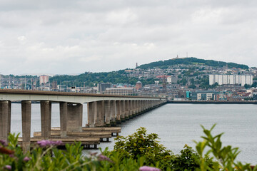 Dundee Scotland: 4th Aug 2024: The Tay Bridge stretches over a calm body of water with a cloudy sky...