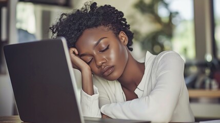Fototapeta premium Exhausted African American woman resting her head on crossed arms while working from home in a cozy indoor space during daylight hours
