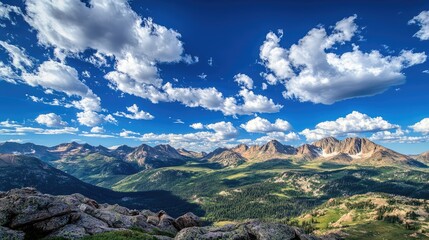A vibrant blue sky with soft clouds scattered above a range of rocky mountain peaks, creating a majestic, peaceful scene