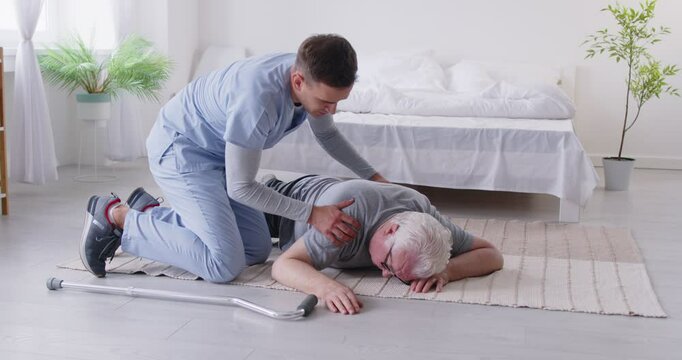 Young male nurse trying to provide first aid emergency helping senior patient lying on the floor with walking stick at home suffering with pain. Nurse support concept. 4k video. Slow motion video.