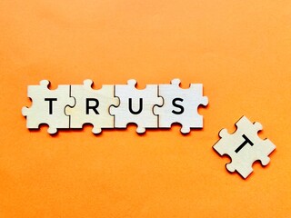 Concept image of broken trust made on wooden puzzle with detached alphabet shot on orange background. Emotion, business, finance, relationship concept design.