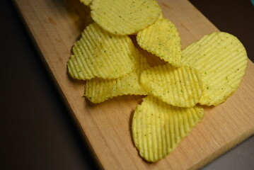 Fast food, not healthy food for human health. Thin slices of potatoes, corrugated chips are located on a light wooden background.