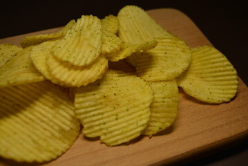 Fast food, not healthy food for human health. Thin slices of potatoes, corrugated chips are located on a light wooden background.