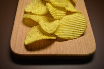 Fast food, not healthy food for human health. Thin slices of potatoes, corrugated chips are located on a light wooden background.