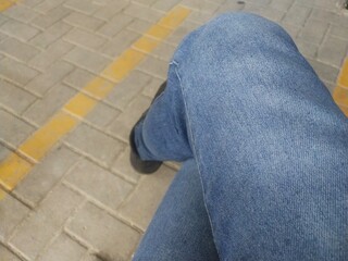 Close up view of a man's legs wearing blue denim pants sitting cross-legged