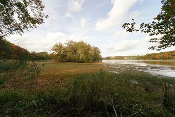A serene landscape featuring a calm lake surrounded by trees and foliage, Kraenepoel Aalter