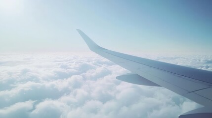 Fototapeta premium A bright midday view of the sky from an airplane window, with the airplane wing cutting across a sea of white clouds below