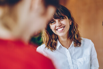 Curly woman with wide smile looking at colleague in multiracial group of people
