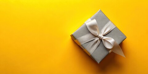A sleek grey gift box tied with a silver ribbon sits atop a cheerful yellow table, composing a striking flat lay perfect for festive occasions and celebrations.