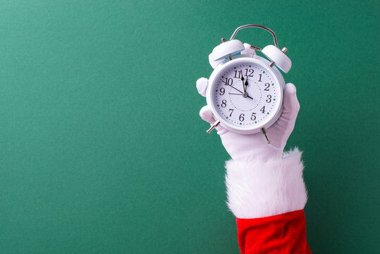 Santa Claus holds an alarm clock, symbolizing the countdown to Christmas on a festive green background. The image evokes holiday anticipation and excitement