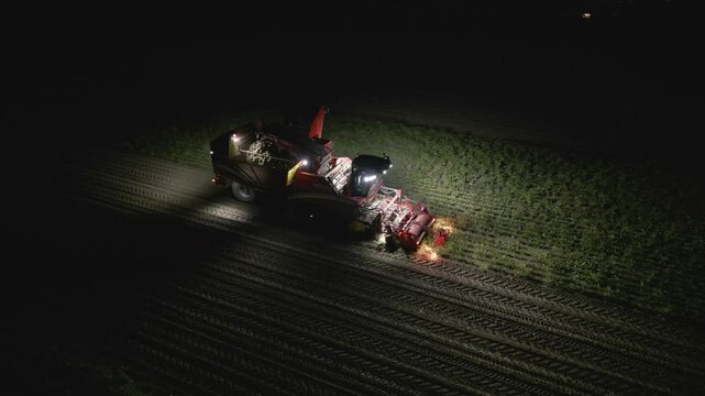 Erntemaschine in Aktion in einem Zuckerr&uuml;benfeld bei Nacht, Luftaufnahme