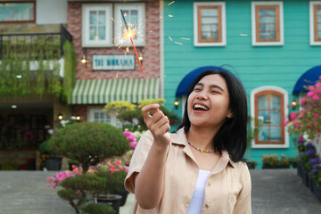portrait of beautiful happy young asian woman holding sparklers fireworks to celebrate new year eve with garden party standing in outdoor vintage house yard