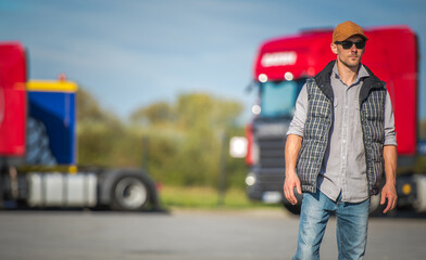 Truck Driver Standing Confidently on a Sunny Day at a Transport Yard With Parked Trucks Nearby