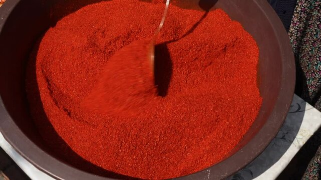 The manufacturer mixes the ground chilli with a wooden spoon, closeup