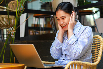 surprised asian woman working on laptop in outdoor cafe covering ears shocked looking at computer