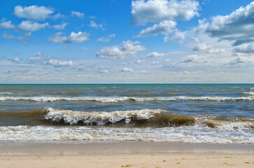 Sea waves wash the beach against a blue sky. Landscape on a wild beach. The sea in the summer.