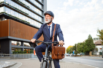 Senior businessman in helmet smiling and looking away while commuting on bicycle to work in city
