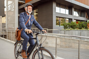 Full length of happy senior man with helmet and bag riding bicycle on street against building in city