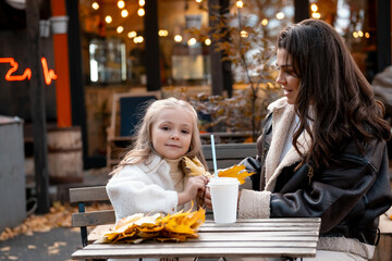 mom and daughter hug, chat and drink coffee in the cafe in autumn, autumn walk, happy family, maternal love