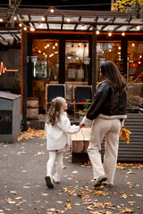 mom and daughter walking with yellow leaves in a cafe in autumn, hugging, autumn walk, happy family, autumn in the city