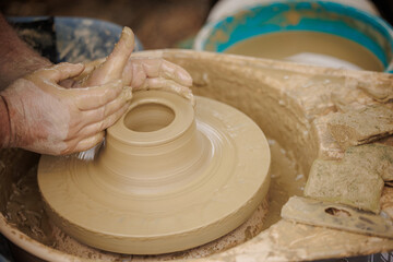 Man potter working on potters wheel making ceramic pot from clay in pottery workshop. 