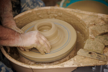 Man potter working on potters wheel making ceramic pot from clay in pottery workshop. 