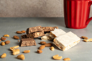 A selection of nougat bars with almonds and peanuts arranged on a surface, accompanied by a red mug in the background, creating a cozy, festive atmosphere.