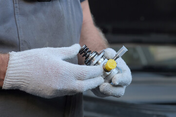 Repair of an automobile engine at a service center. A new high-pressure fuel pump is in the hands of an auto mechanic. Inspection of the new spare part before installation.