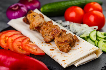 Close up of the pork kebab with vegetables and sauce on lavash