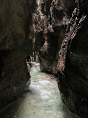 The river winds through the rocky valley of Partnachklamm Gorge, carving its way between towering cliffs and creating a stunning natural landscape in the Bavarian Alps.