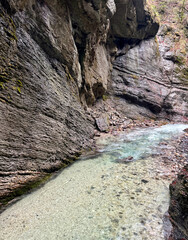The beautiful stream flows through the rocky valley of Partnachklamm Gorge, where lush moss clings to stones, creating a vibrant and serene natural scene in Garmisch-Partenkirchen.