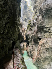 The beautiful stream flows through the rocky valley of Partnachklamm Gorge, where lush moss clings to stones, creating a vibrant and serene natural scene in Garmisch-Partenkirchen.