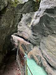 A narrow walkway winds through the rock cliffs at the valley's base alongside a flowing stream at Partnachklamm Gorge, Garmisch-Partenkirchen, offering a stunning alpine experience.