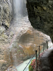 A narrow walkway winds through the rock cliffs at the valley's base alongside a flowing stream at Partnachklamm Gorge, Garmisch-Partenkirchen, offering a stunning alpine experience.