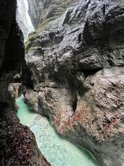 The beautiful stream flows through the rocky valley of Partnachklamm Gorge, where lush moss clings to stones, creating a vibrant and serene natural scene in Garmisch-Partenkirchen.